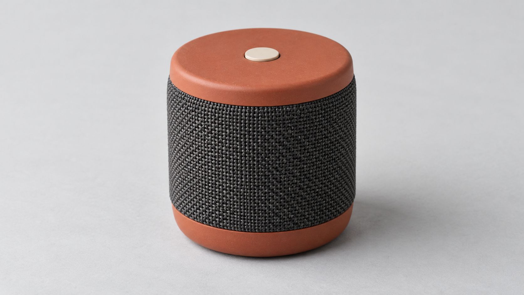 Terracotta cylindrical portable speaker with a charcoal woven grille and one ivory button on top.