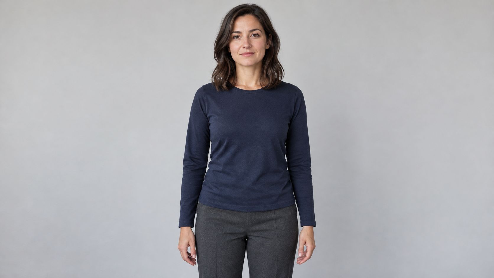 Fictional woman in a navy shirt and charcoal trousers, with both hands visible against a gray background.